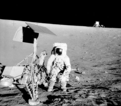 Astronaut op de maan naast een lander en in de verte nog een lander.